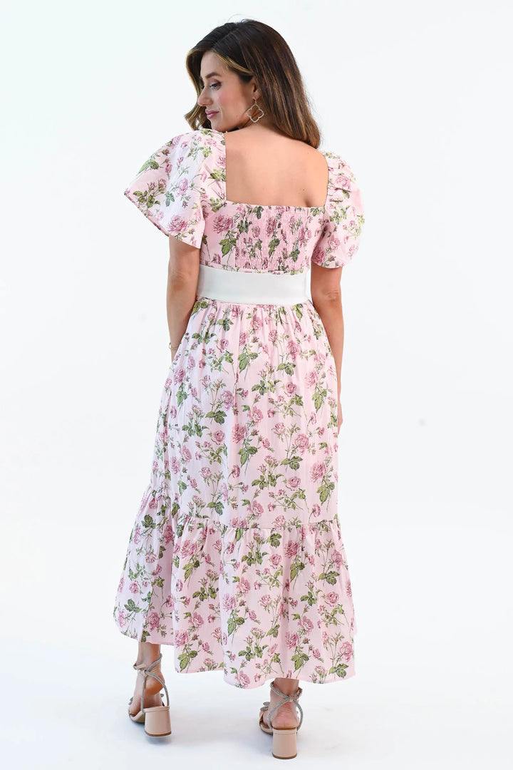A woman wearing a pink floral puff sleeve maxi dress with a waist tie belt and side slit, styled with elegant heels