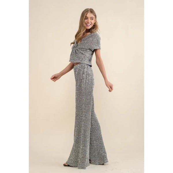 Model in a silver sequin two piece pants set: twist-front cropped short-sleeve top and high-waisted wide-leg pants, side view