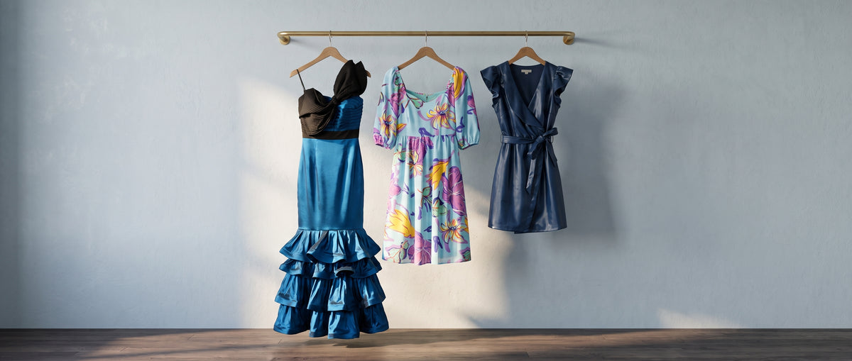 A teal satin mermaid gown, a light blue floral puff-sleeve dress and a navy faux-leather wrap dress on a brass rail against a blue-grey wall