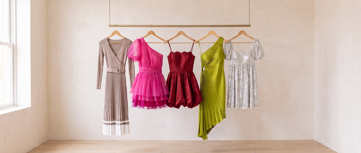 Five dresses on a brass rail: a taupe pleated sweater dress with a D-ring belt, a hot pink one-shoulder tulle mini, a red satin scallop bubble mini, a lime pleated one-shoulder high-low dress and a silver sequin babydoll mini