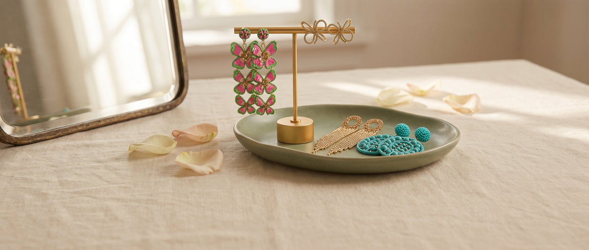 Pink butterfly, gold bow, gold fringe and turquoise beaded earrings on a gold stand and a sage dish on a linen table