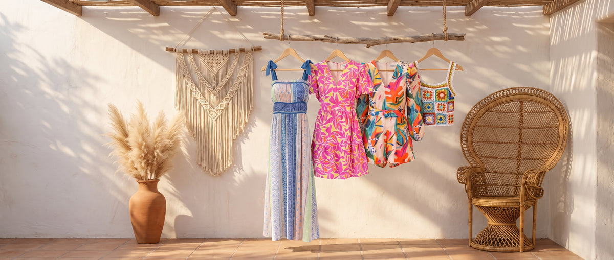 Striped maxi dress, pink print dress, bright floral romper and crochet tank on a driftwood rail beside macramé and a peacock chair