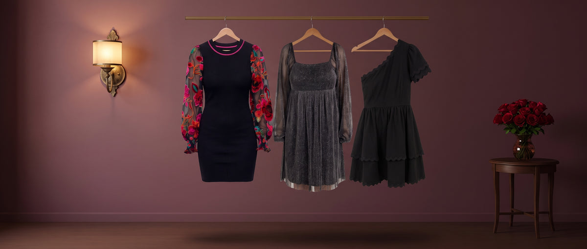 Three black dresses, one with red floral sheer sleeves, on a brass rail against a plum wall with a glowing sconce and red roses