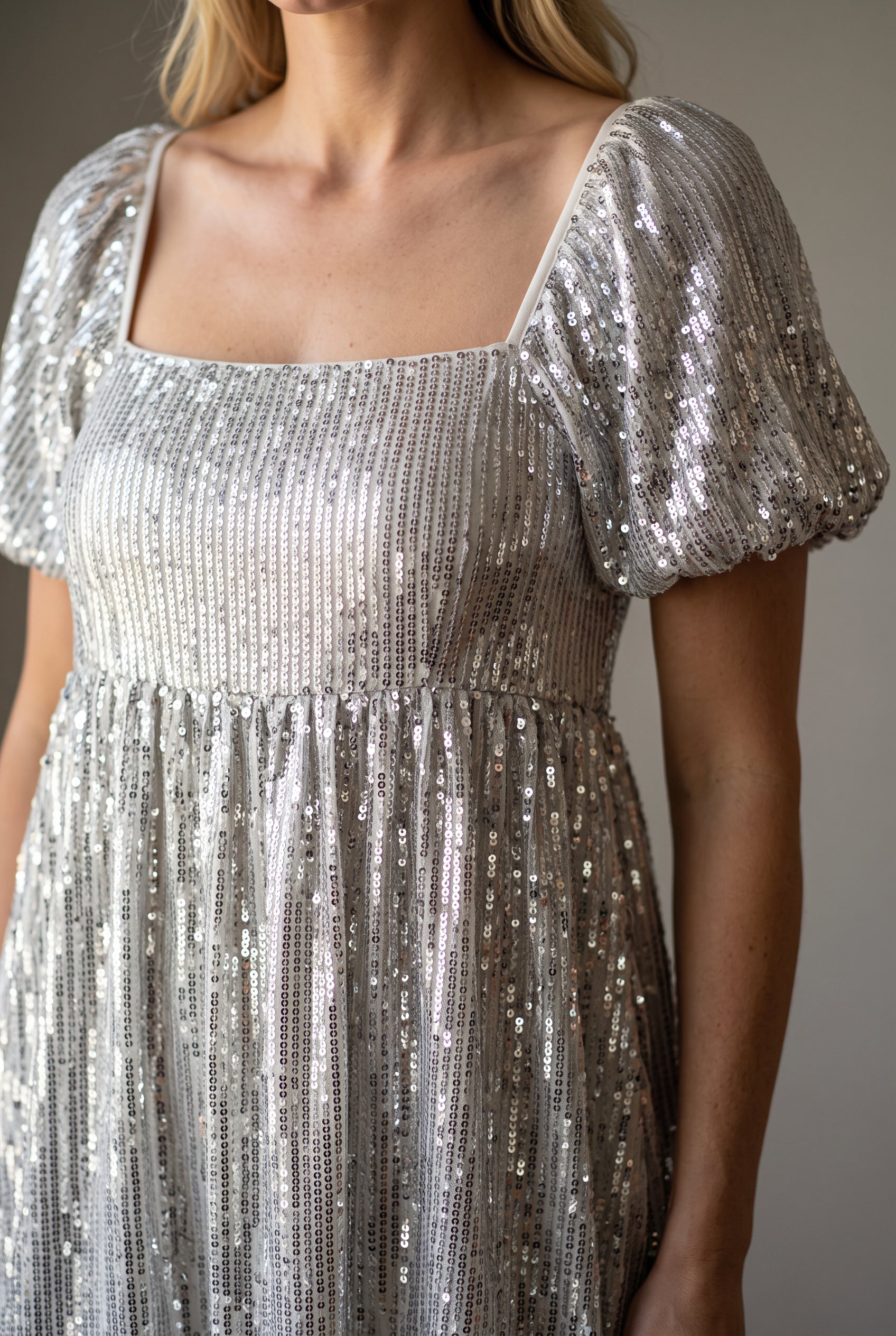 Close detail of the silver sequin dress showing vertical sequin rows, puff sleeve and empire seam.