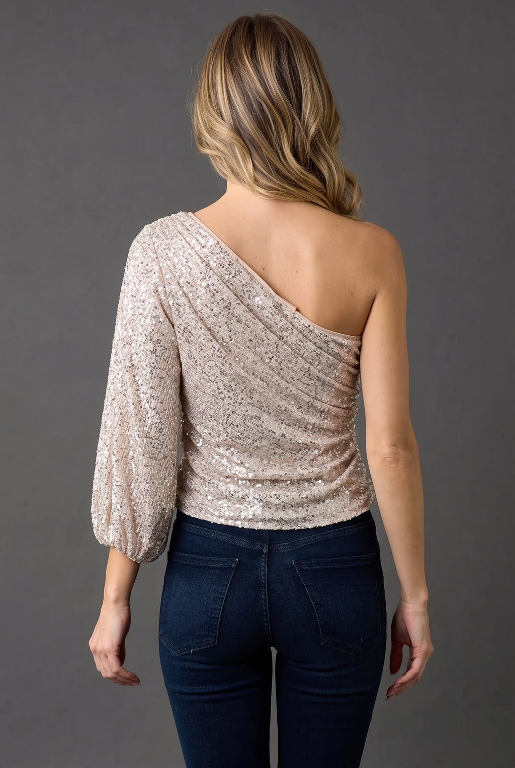 Straight back view of the champagne one-shoulder sequin top showing its diagonal open neckline.