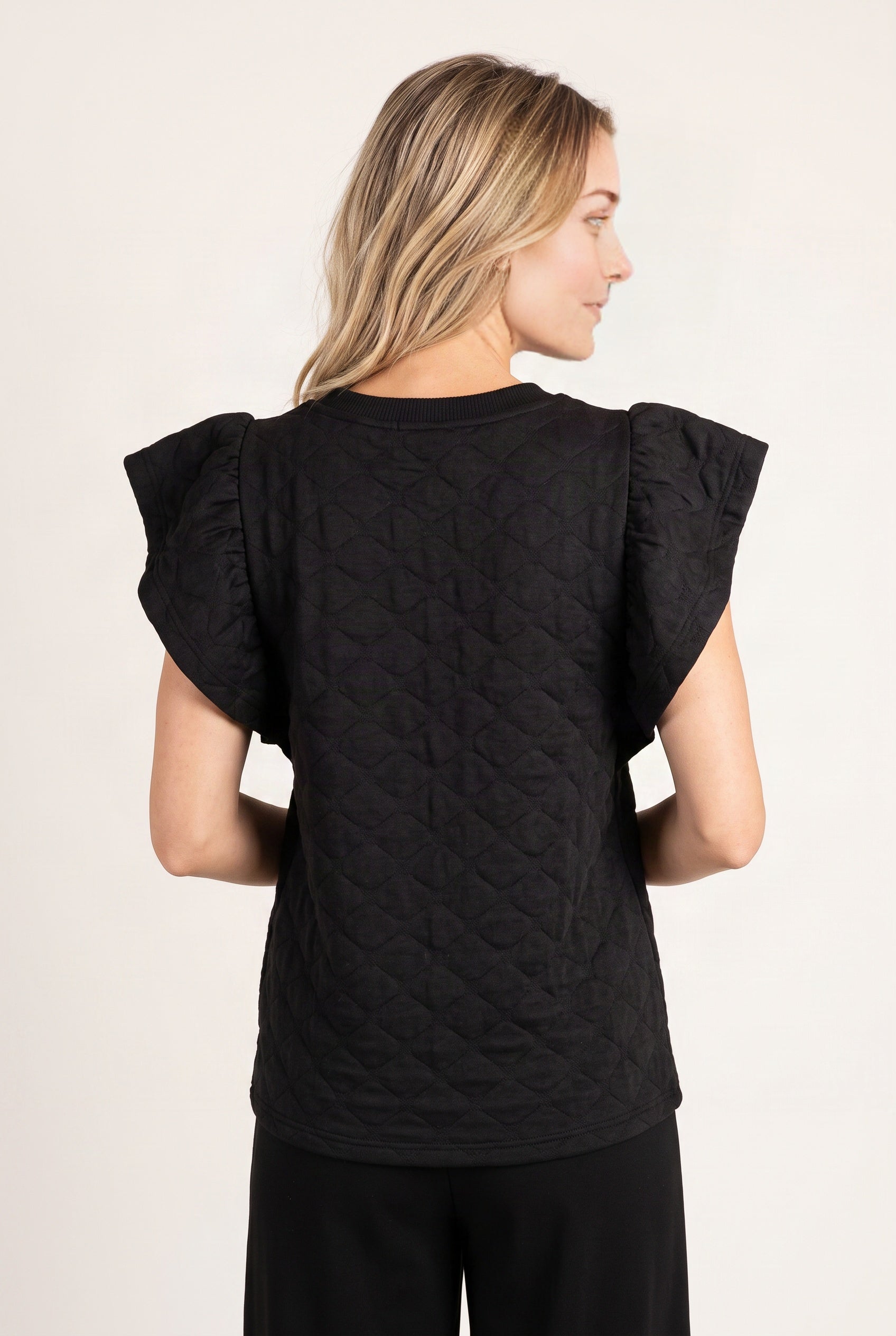 Back view of the black ruffle sleeve top showing its textured back, layered shoulders and full hem.