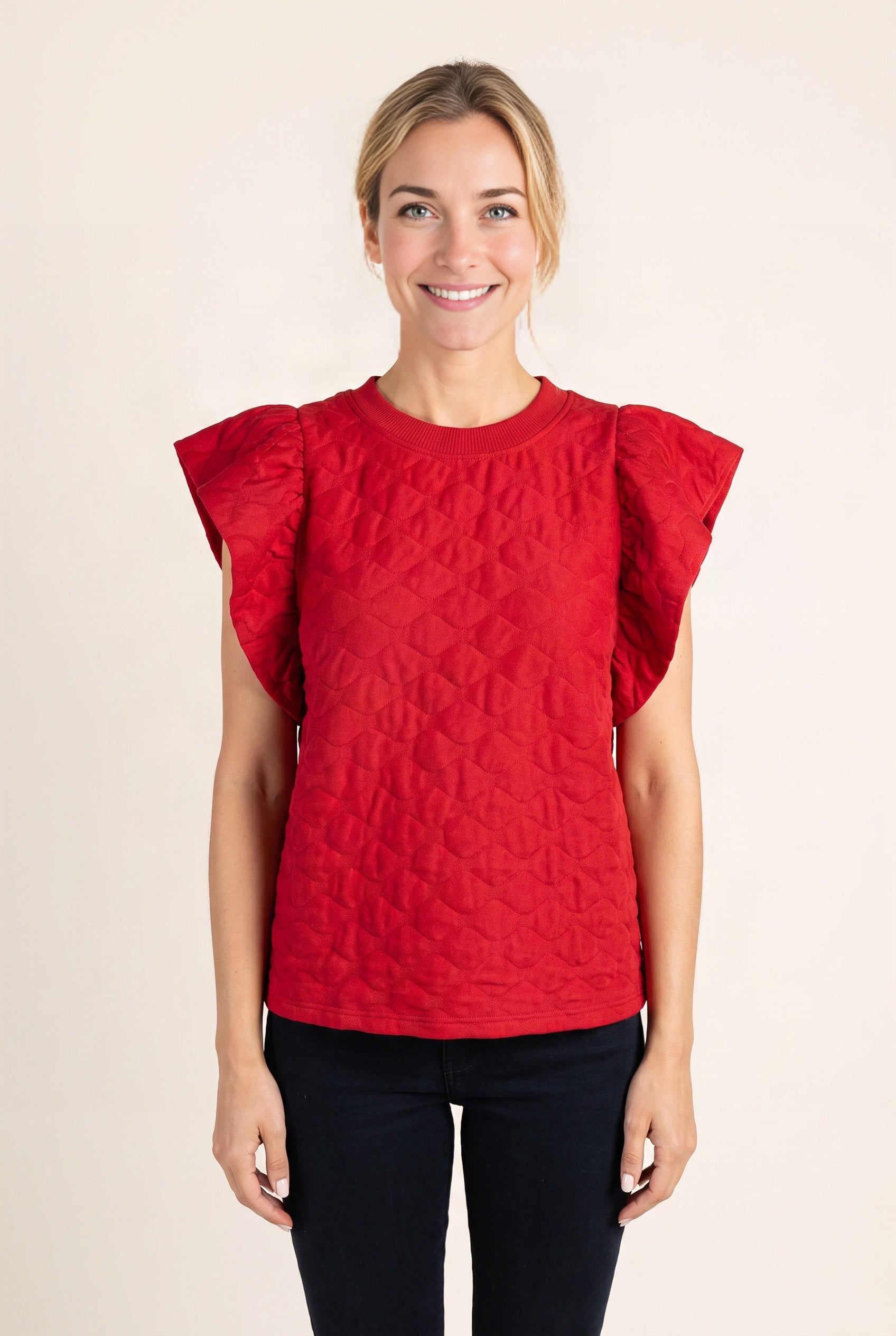 Close view of the black top showing its raised tonal pattern, ribbed neckline and double ruffle sleeve.