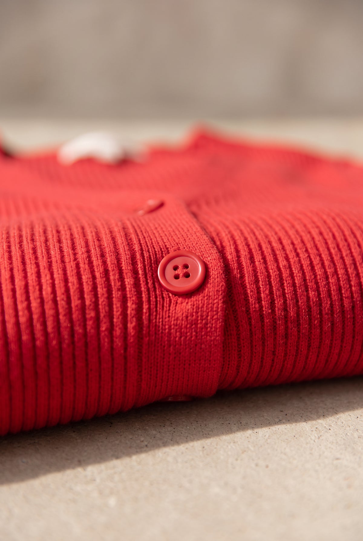Red cardigan close-up showing the fine rib knit, tonal button and narrow front band.