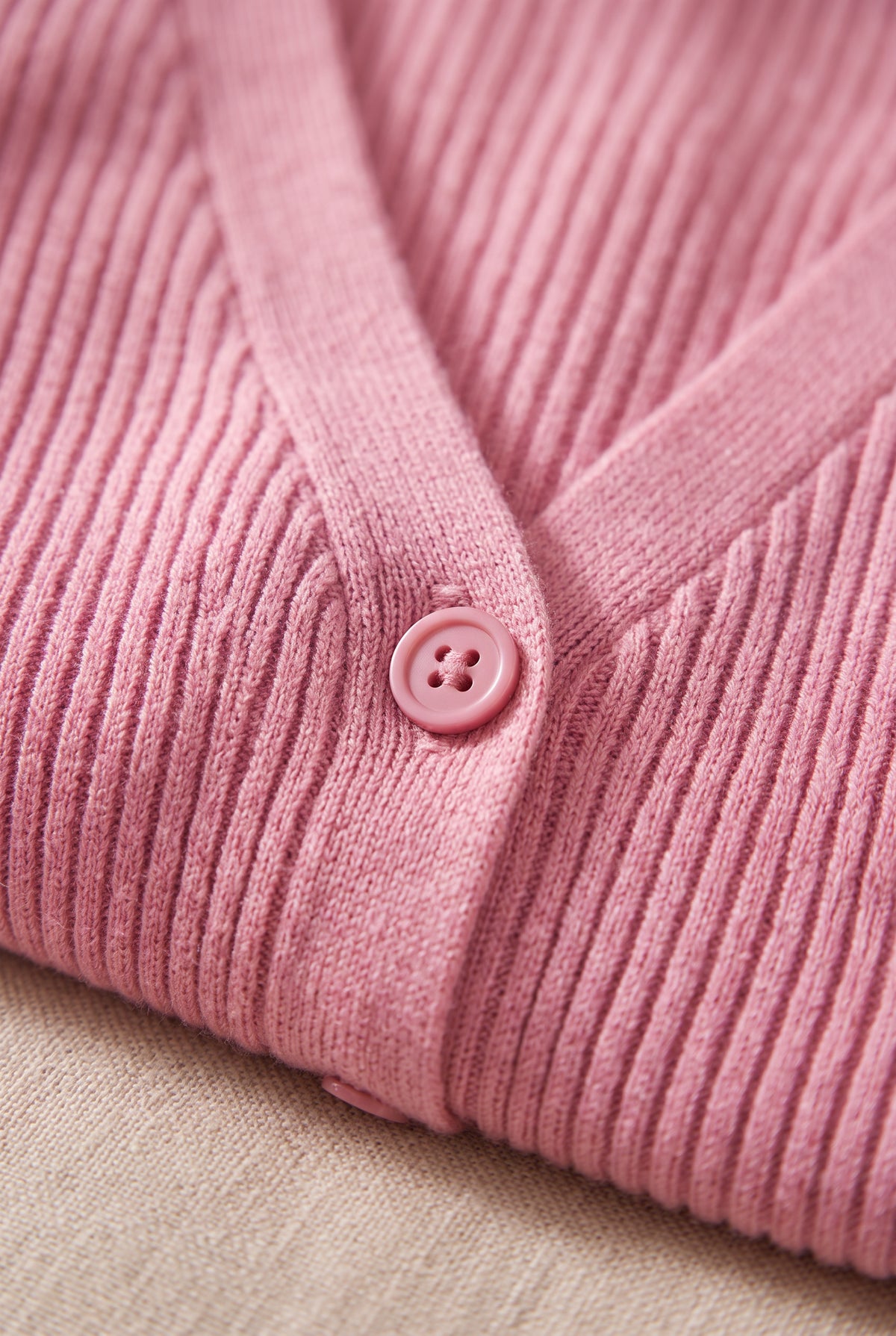 Pink cardigan close-up showing the fine rib knit, tonal button and narrow front band.