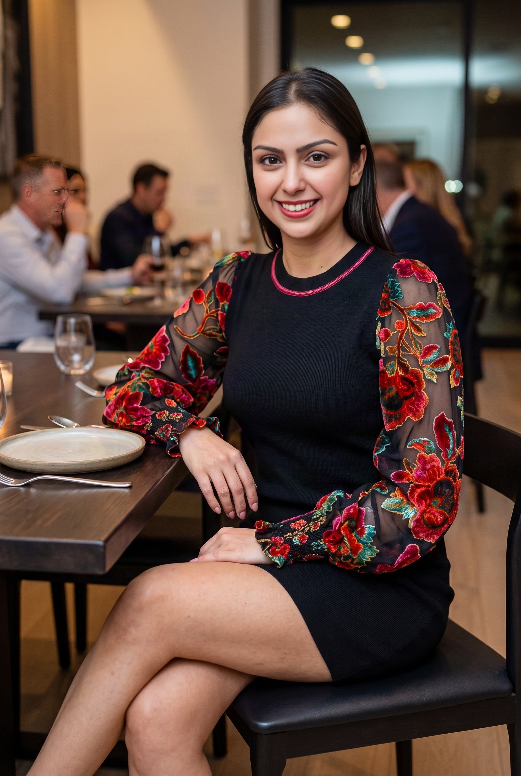Shweta wearing the black floral-sleeve sweater dress while seated at an elegant dinner table.