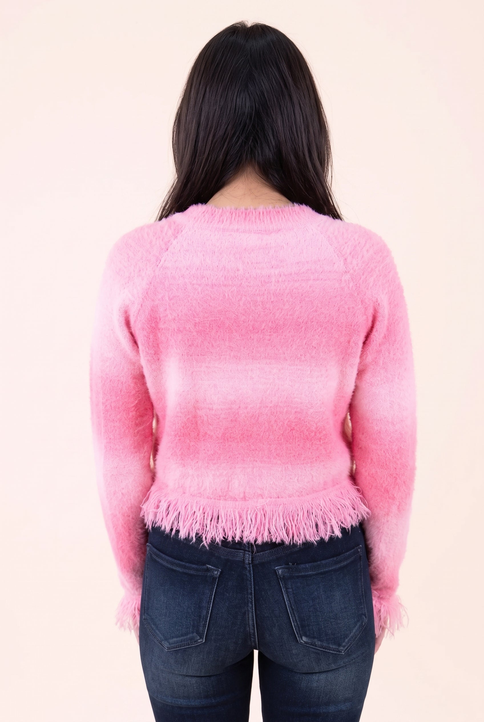 Back view of the pink cropped cardigan showing its plain back, shoulder shaping and fringed hem.