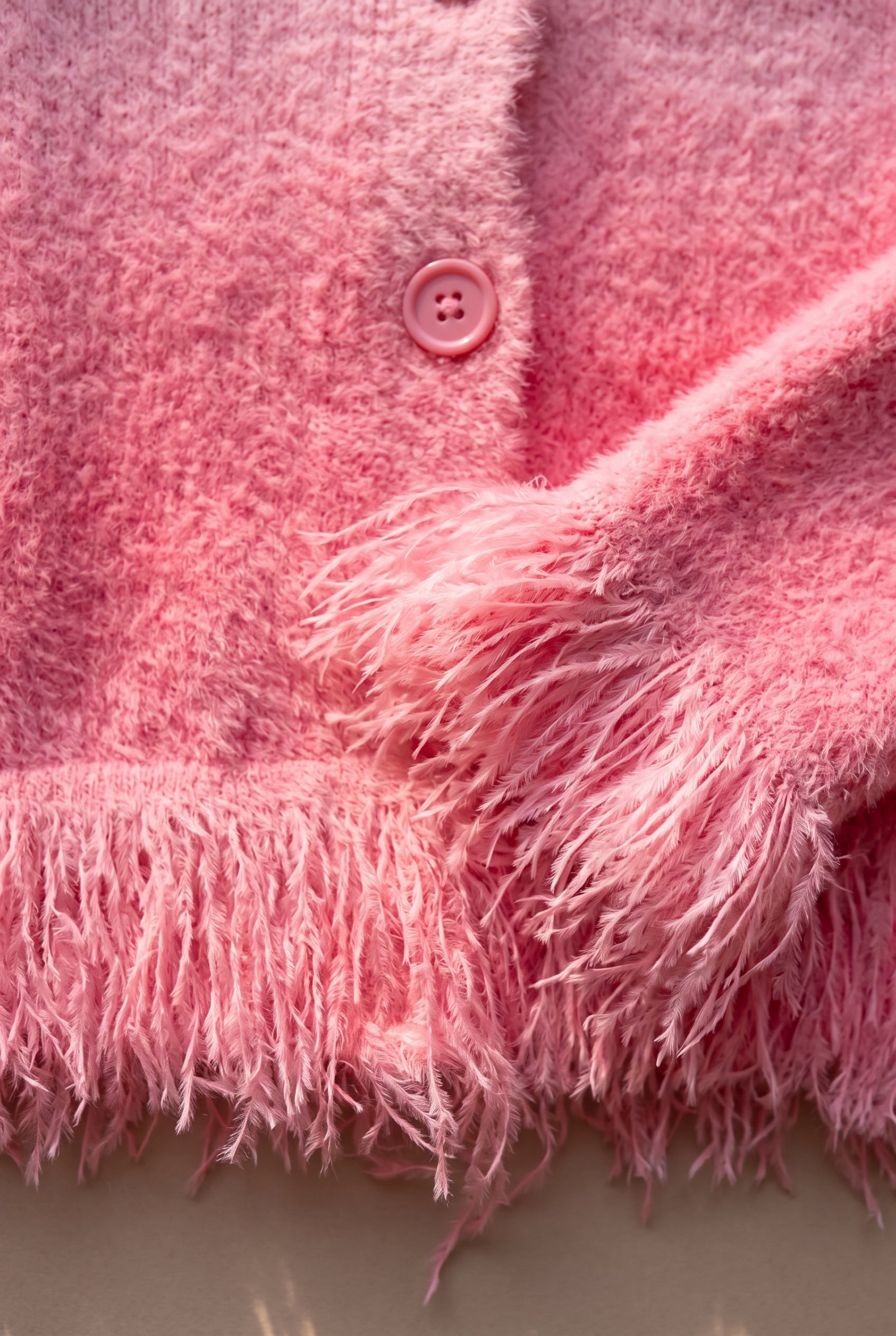 Close view of the pink cardigan showing its fuzzy pile, tonal button and long fringe trim.