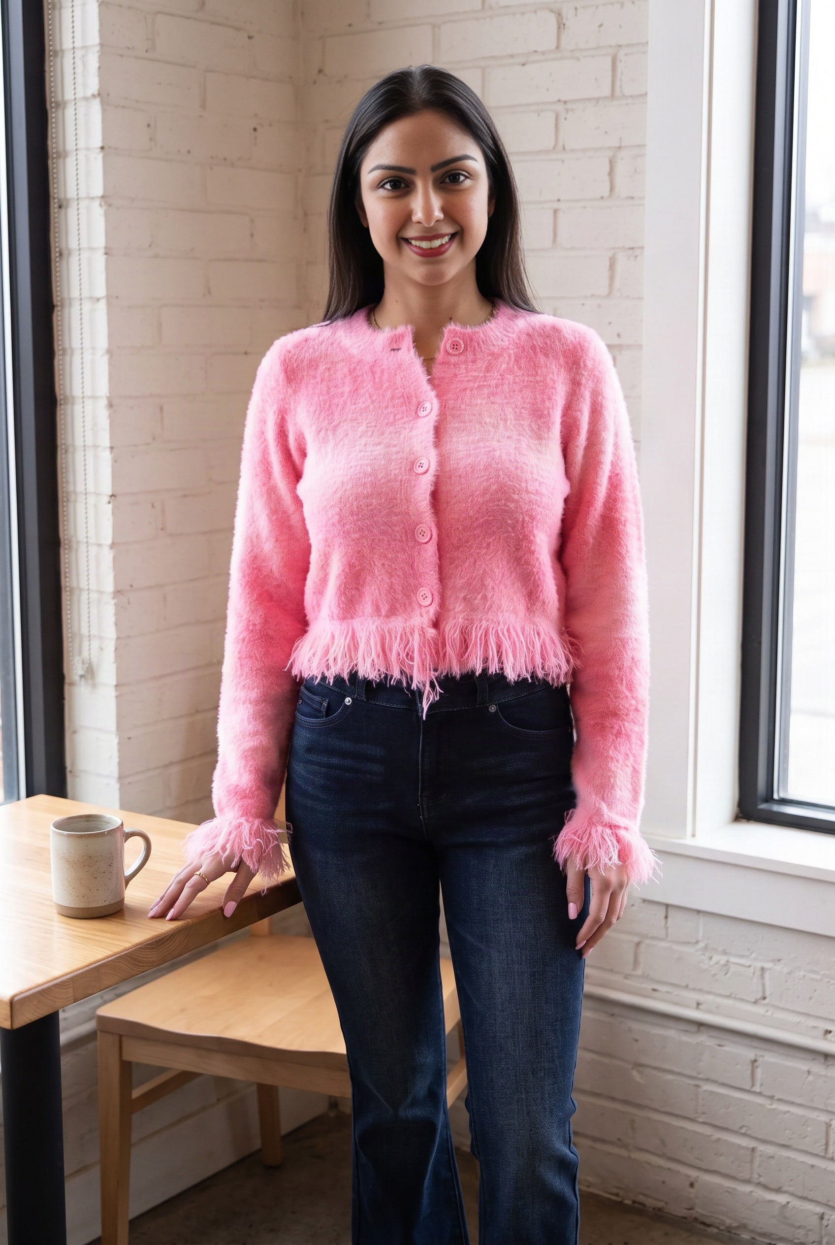 Shweta styles the pink fuzzy cropped cardigan with dark jeans in an everyday café setting.