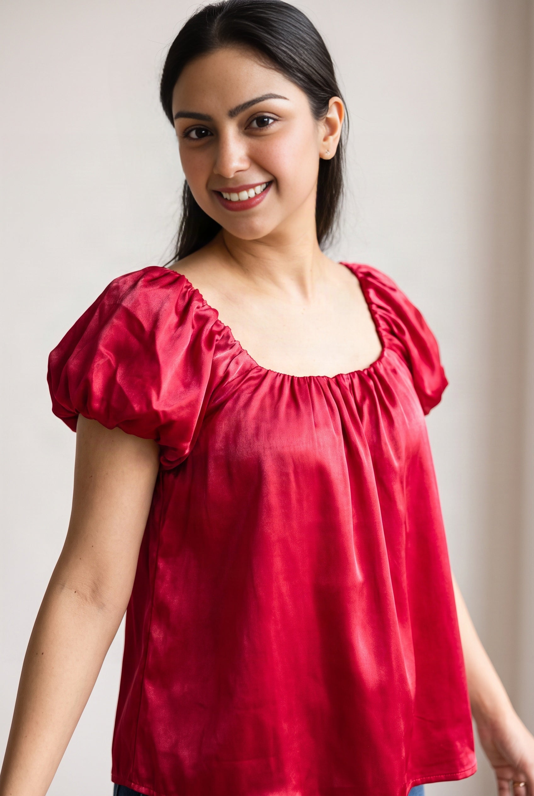 Close view of the red satin top showing its sheen, gathered square neckline and puff sleeve construction.