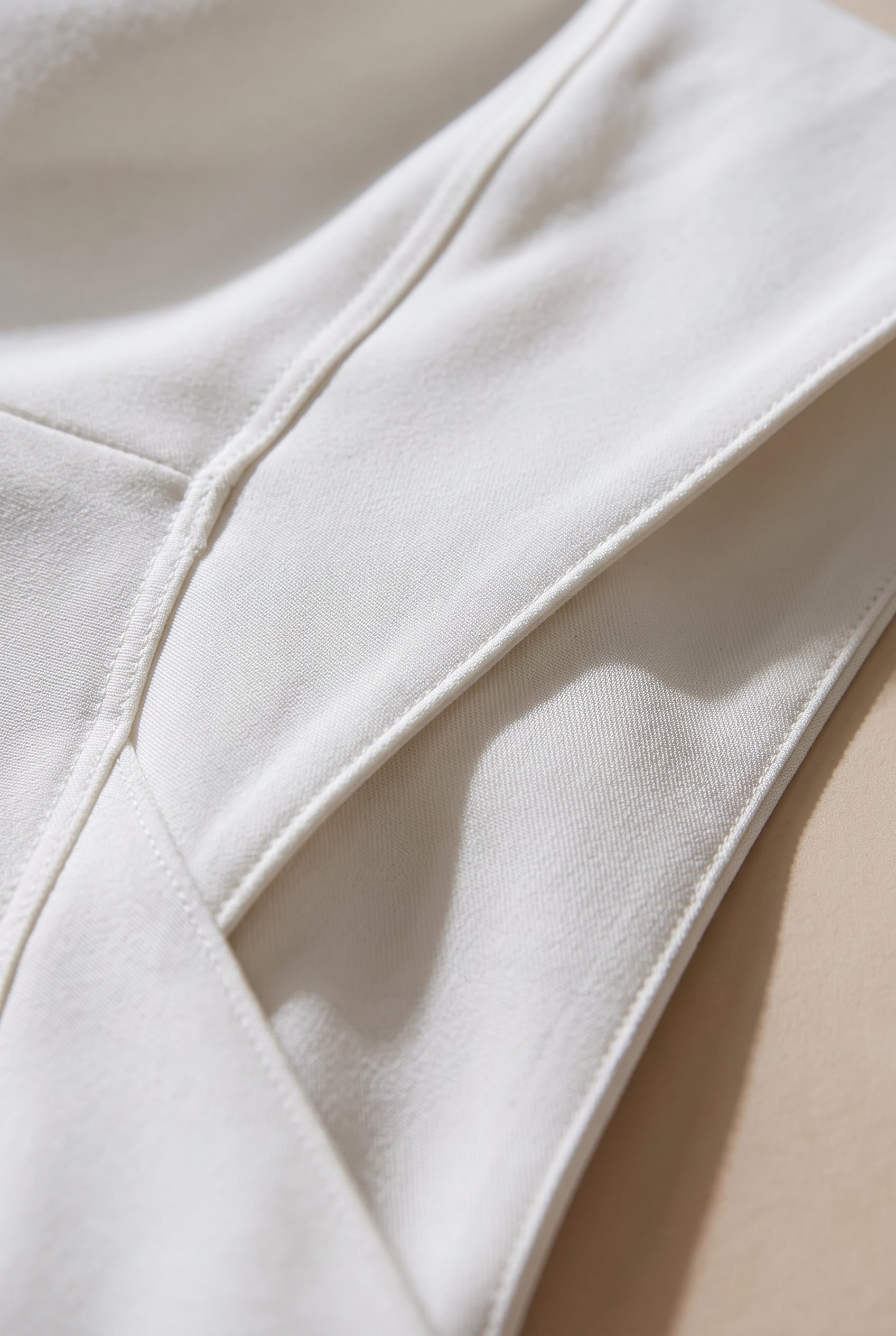 Close-up of the cream flare jeans showing the crossover waistband seam and smooth fabric surface.