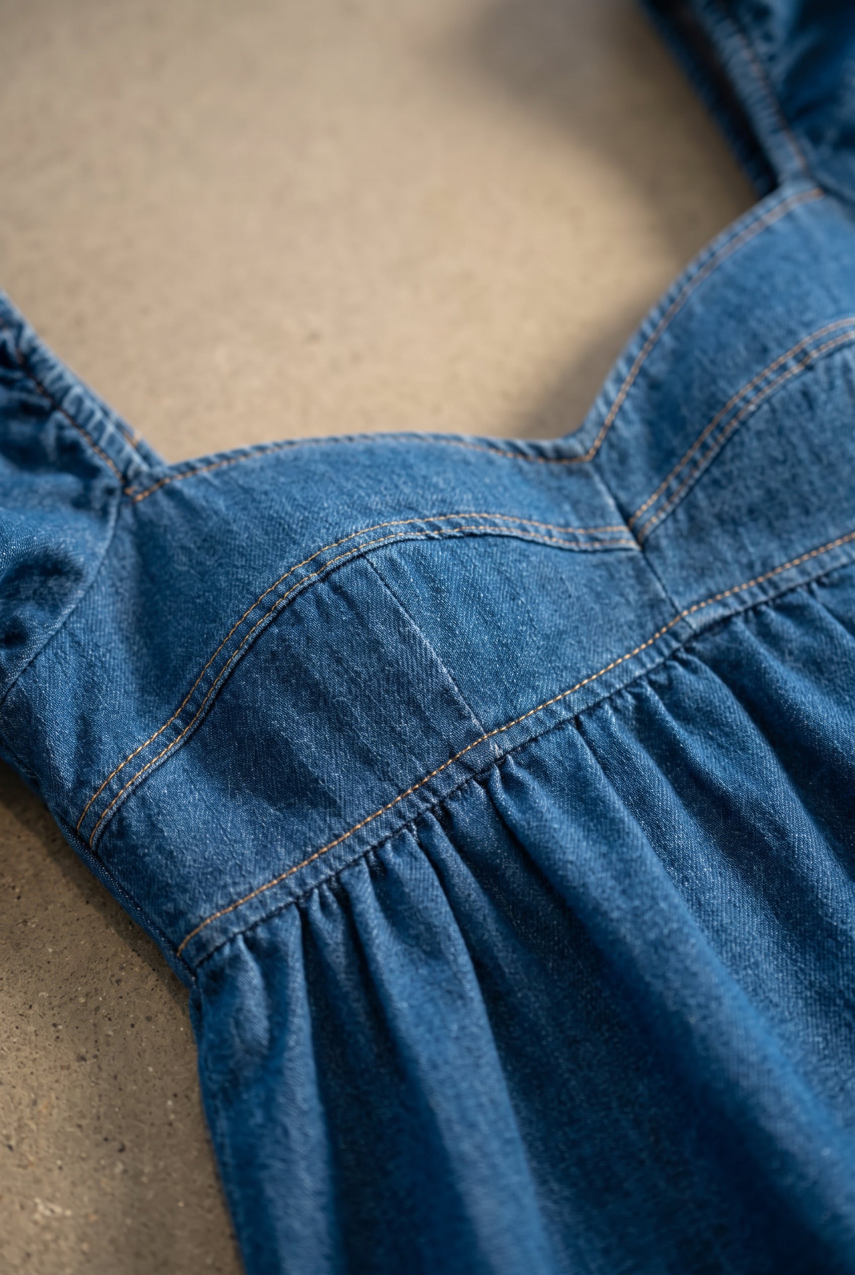 Close detail of the blue denim dress showing sweetheart topstitching, cup seams, and gathered empire seam.