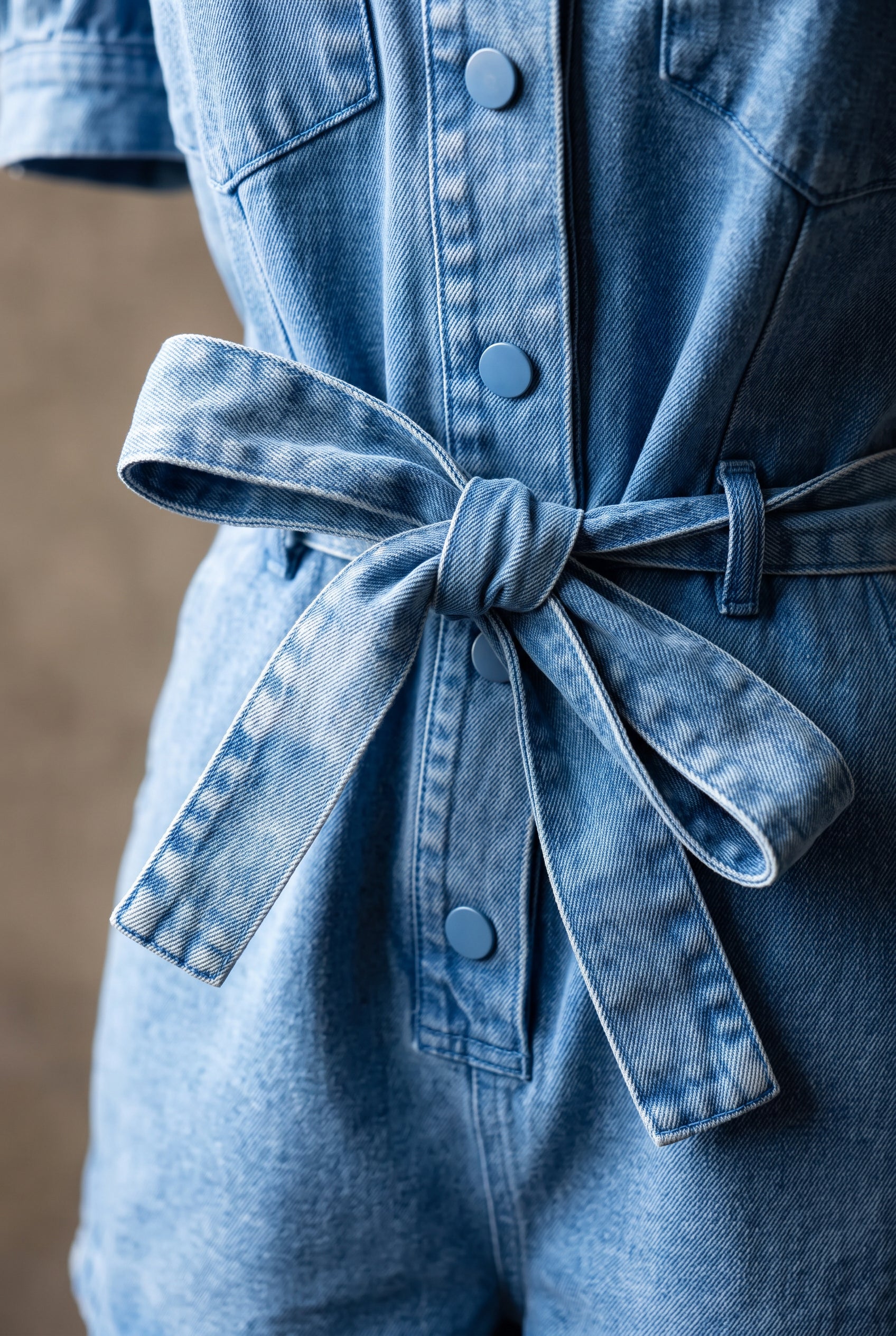 Close detail of the romper’s washed denim, self-fabric belt and tonal front snap.