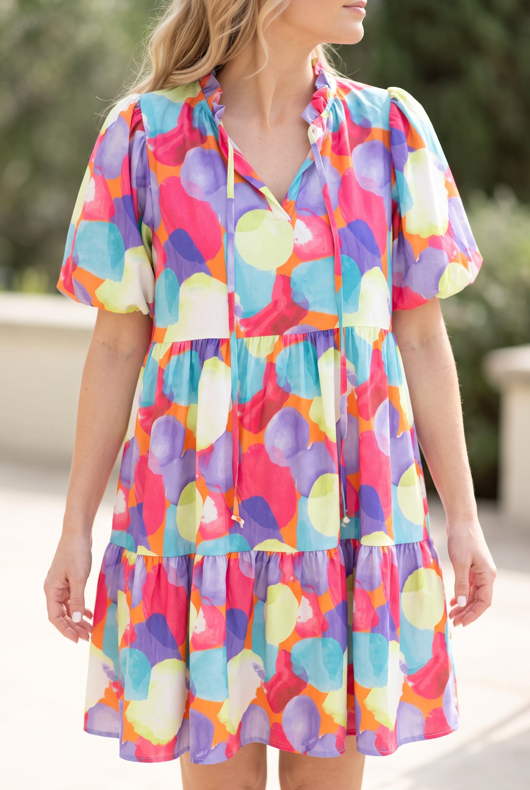Close view of the dress’s ruffled V-neck, long ties, gathered waist and multicolor watercolor print.