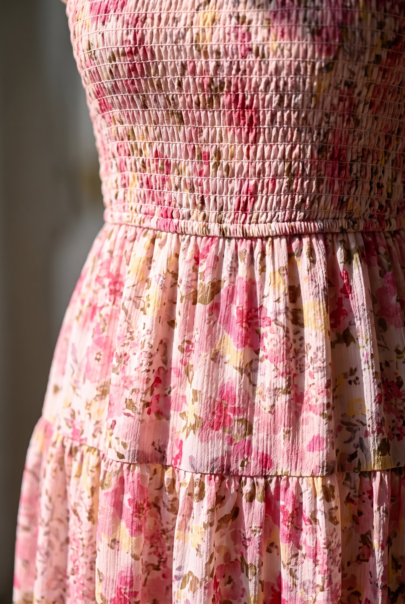Close detail of the pink floral dress showing its elastic smocking, waist seam and softly crinkled fabric.