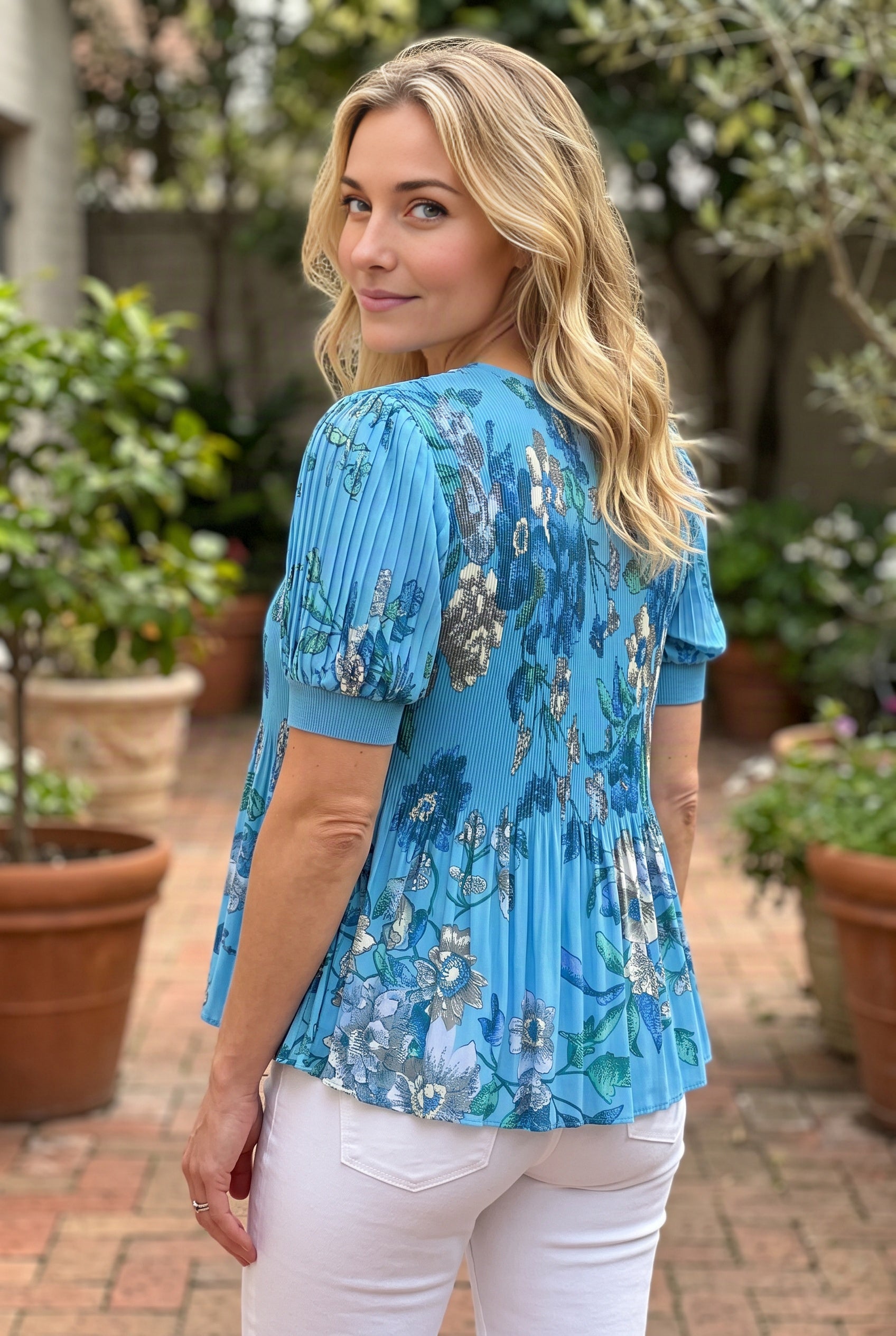 Back drape of the Wherever You Went pleated top showing its neckline, pleats and untucked flared hem.