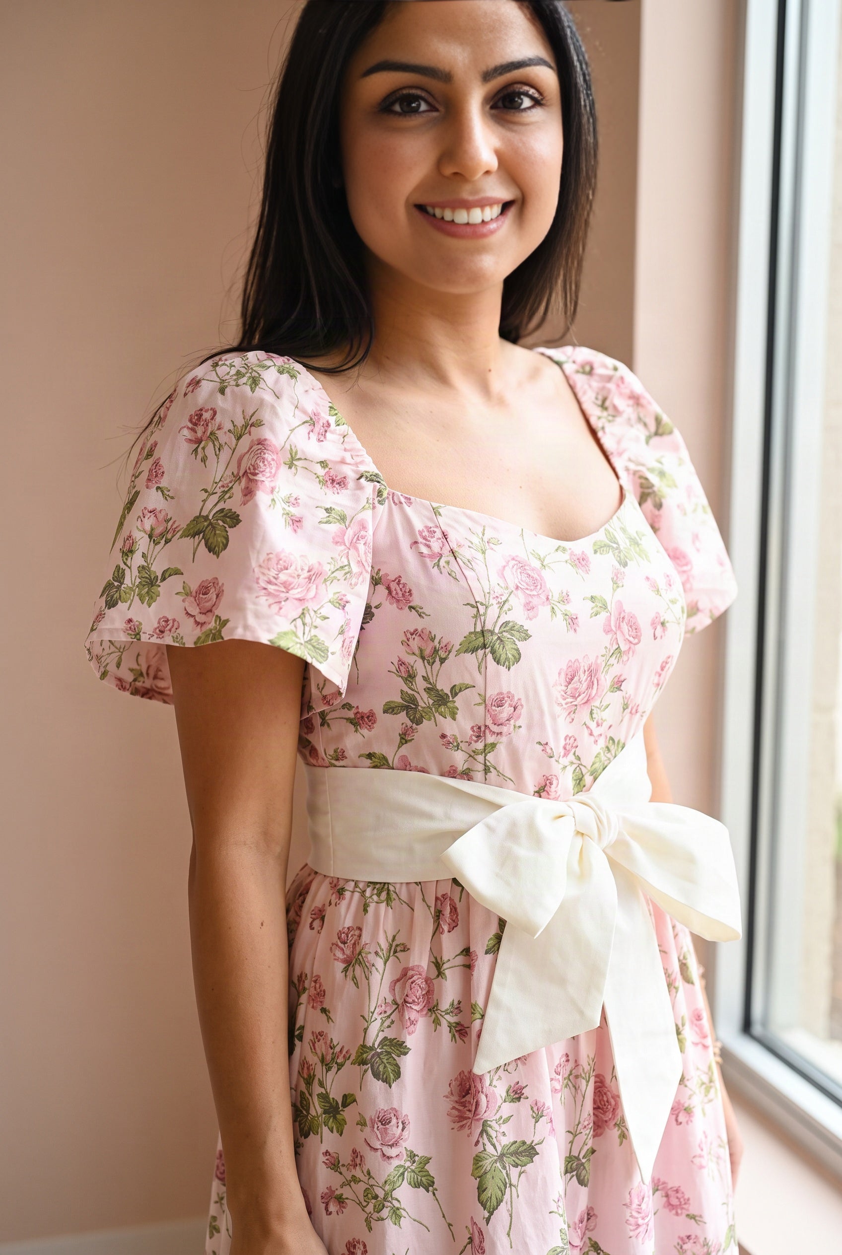 Bodice detail of the pink floral maxi dress showing the flutter sleeve, floral folds, seams, and ivory bow.