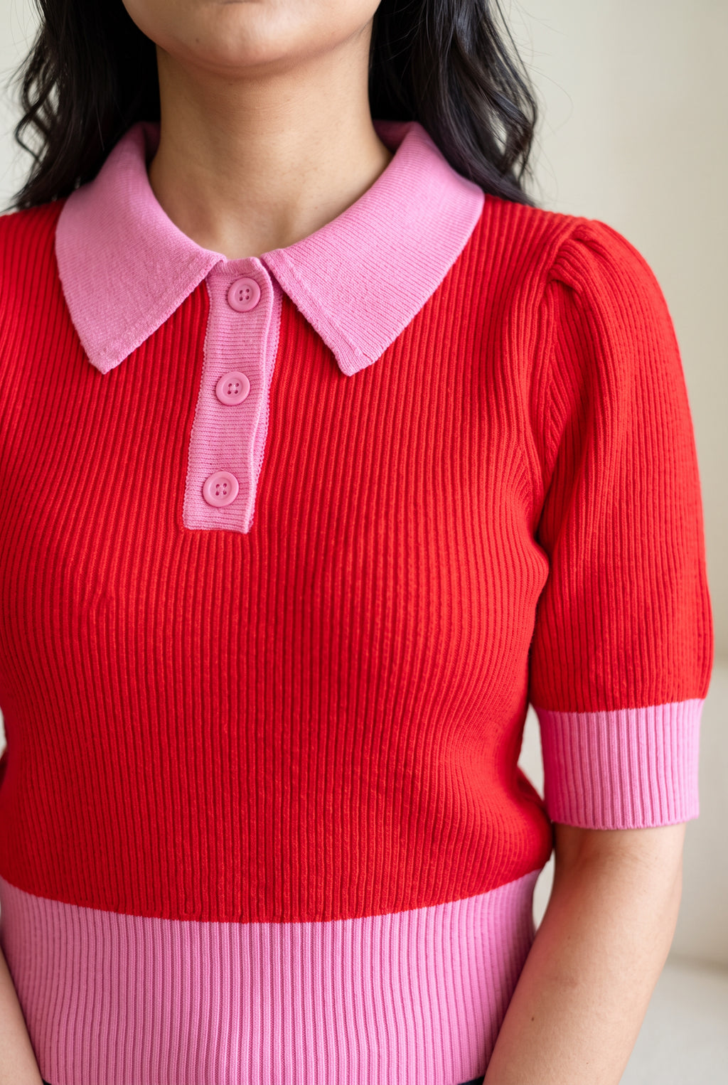 Close view of the sweater's pink collar, three-button placket, cuff, and red rib knit.