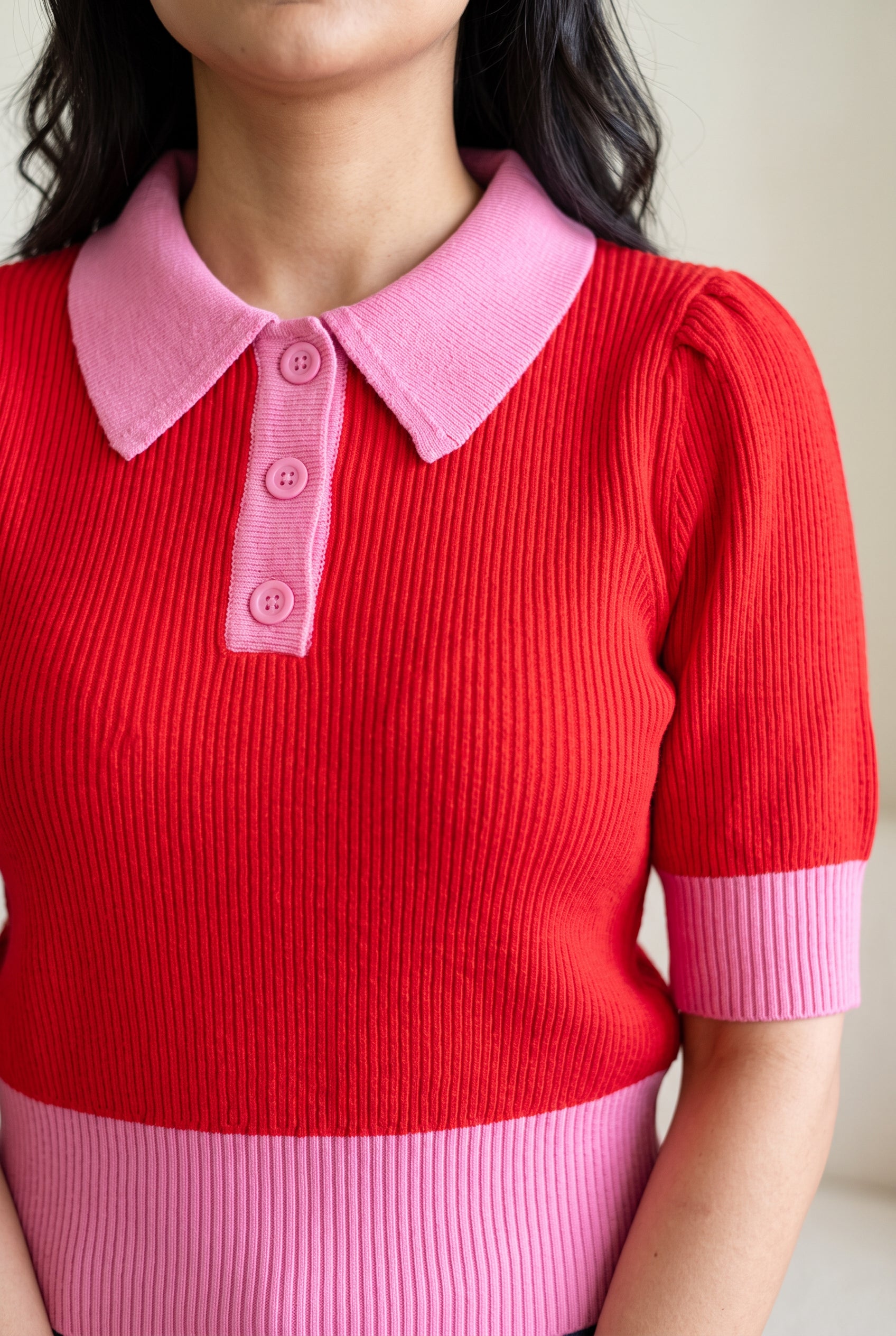 Close view of the sweater's pink collar, three-button placket, cuff, and red rib knit.