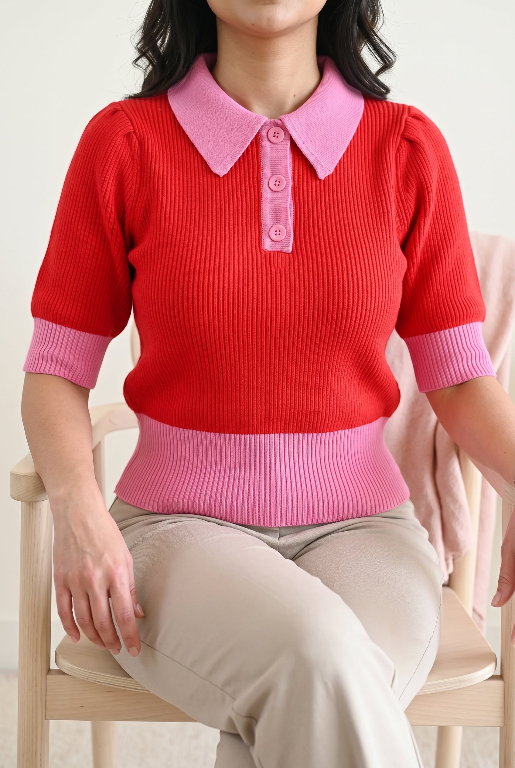 Seated everyday styling of the red and pink sweater showing the waistband and sleeves at rest.