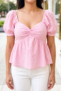 Close detail of the pink gingham top showing its raised cotton check, front twist and sleeve translucency.