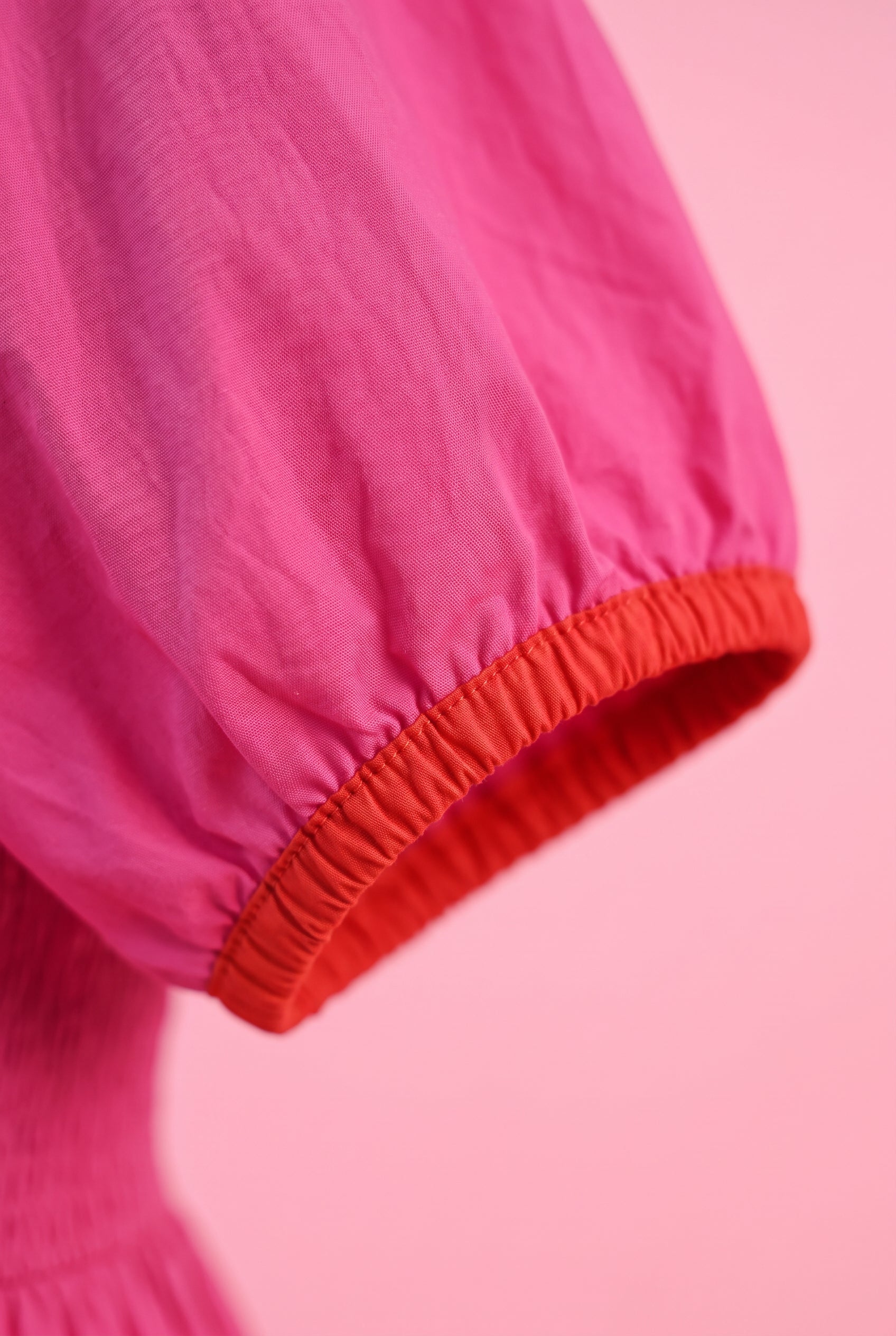Close detail of the Small Magenta dress showing the pink fabric, red cuff, gathering and seam finish.