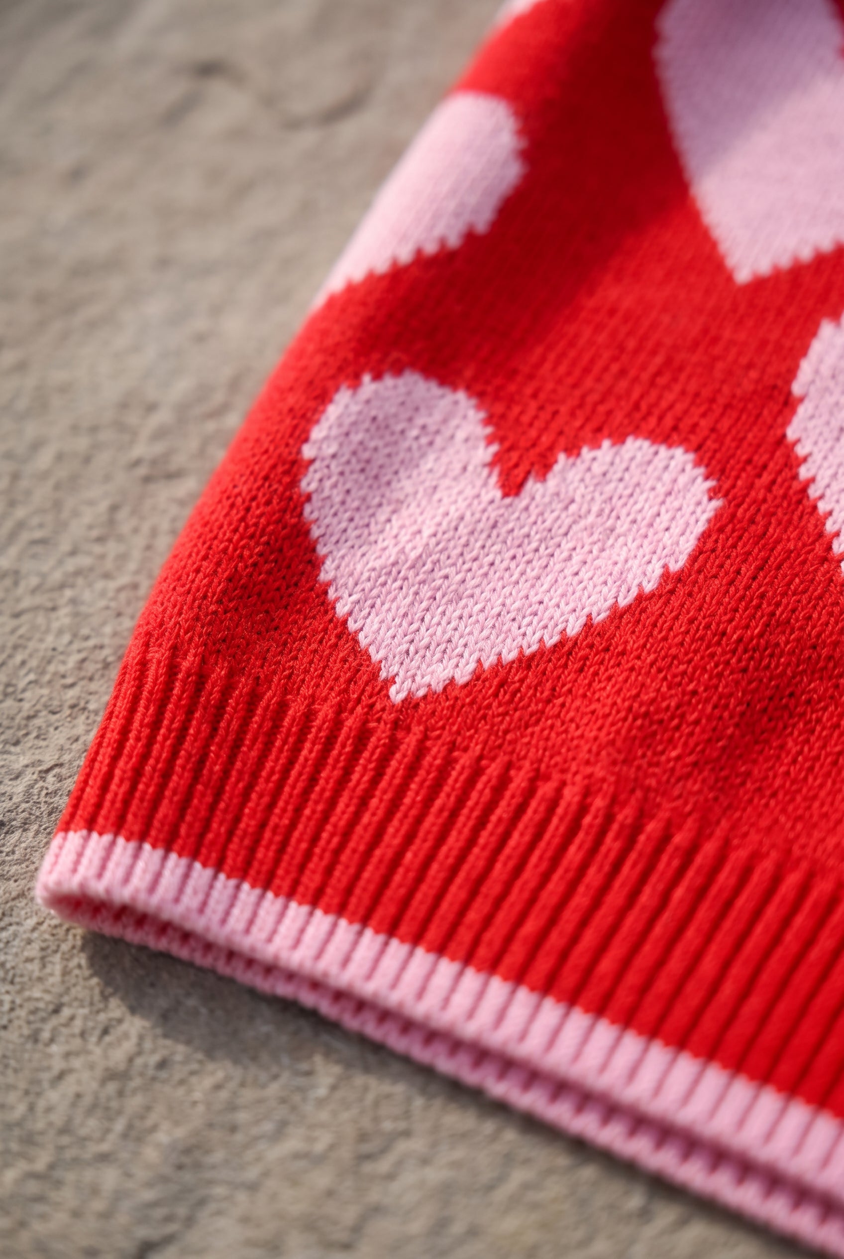 Macro detail of the red and pink heart sweater showing knitted-in colorwork and pink-tipped ribbing.