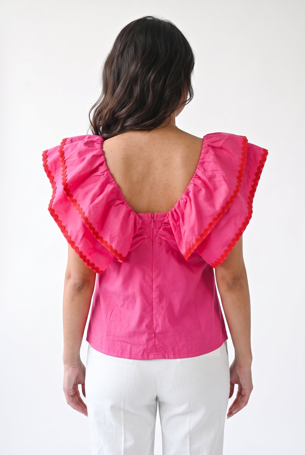 Pink ruffle babydoll top styled with white trousers in a bright everyday studio setting.