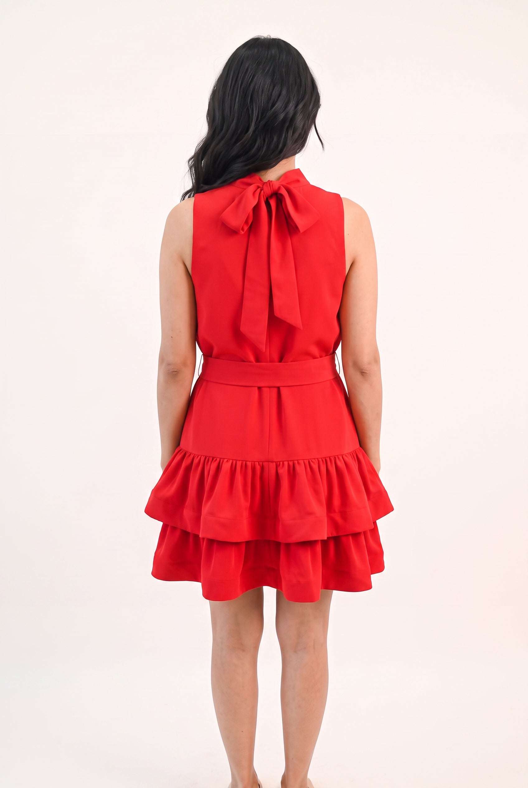 Back fit of the red ruffle mini dress showing its neck bow, waist sash and tiered skirt.
