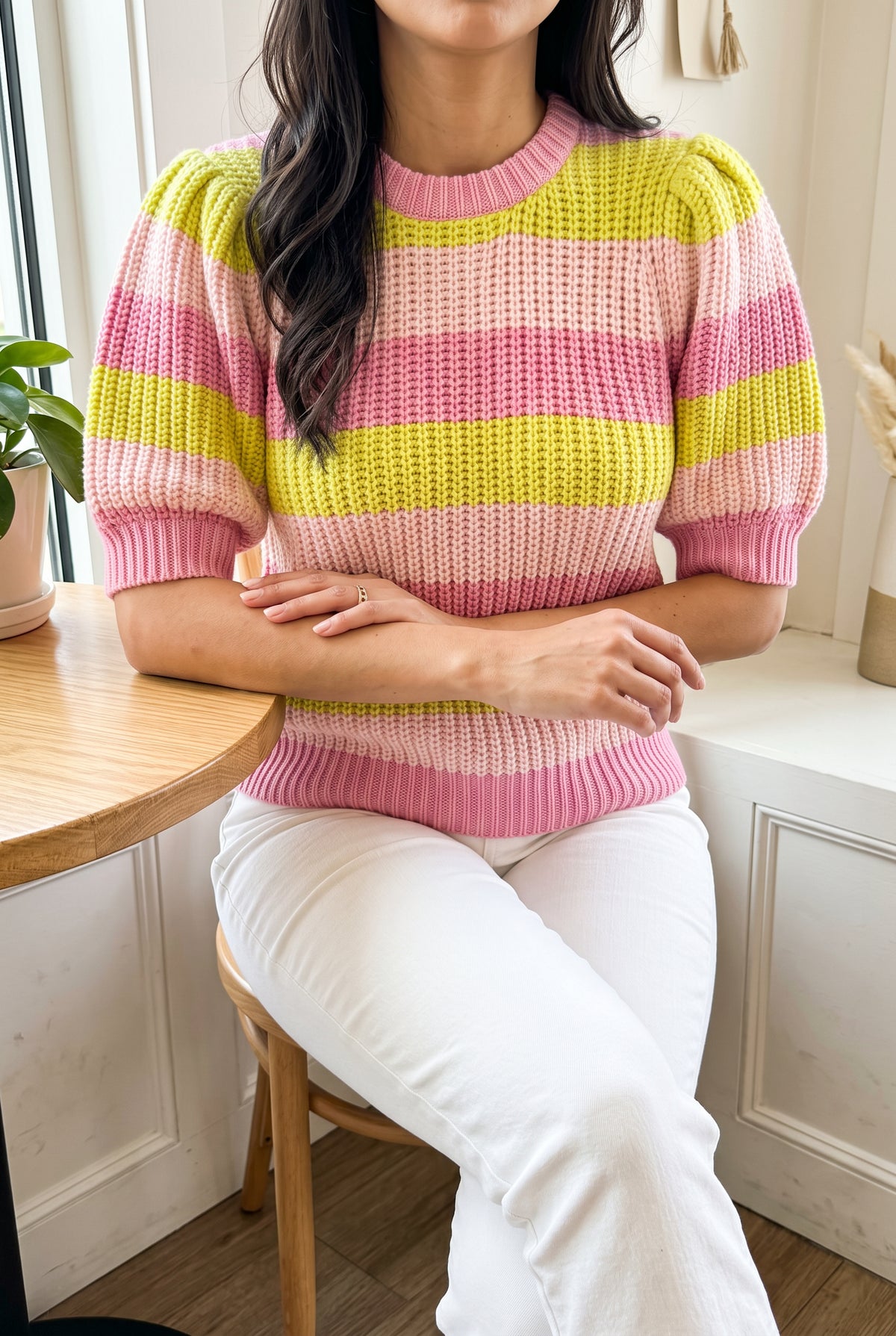 Share Your Story Sweater Top in Small worn seated at a café with white pants.