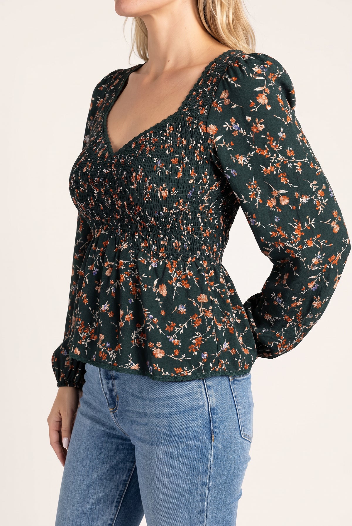 Angled side fit of the floral top showing its fitted smocked bodice and flared peplum.