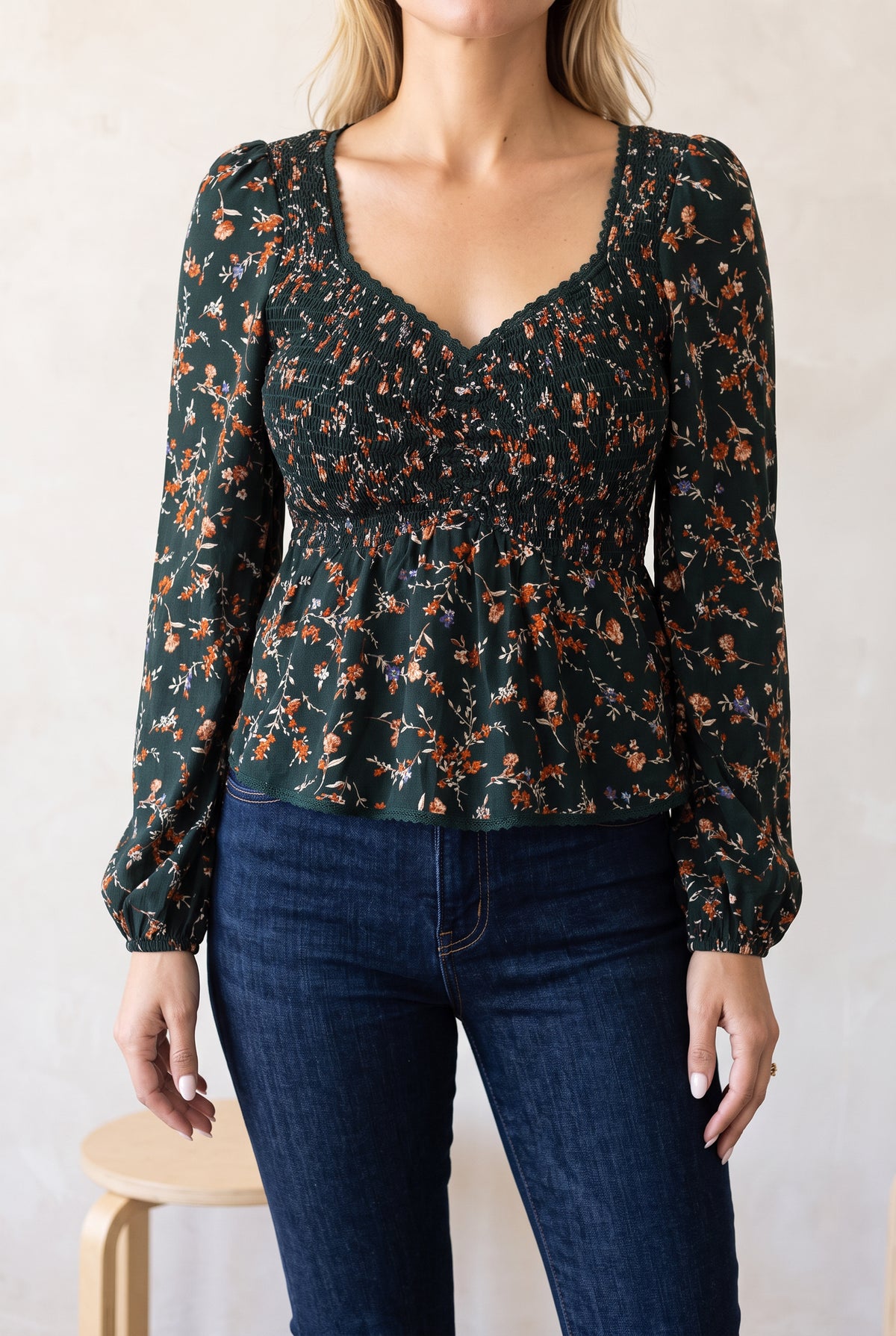 Bright studio styling of the floral peplum top worn untucked with dark high-rise jeans.