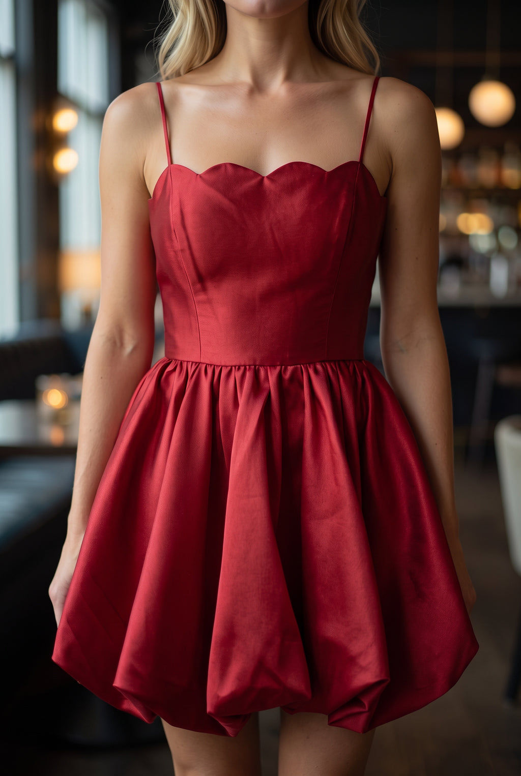 Close view of the red dress showing its scalloped neckline, fine straps, bodice seams and satin sheen.