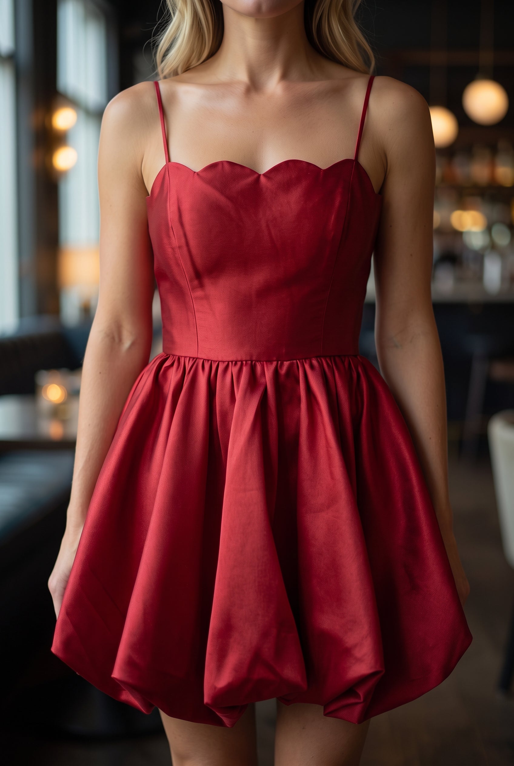 Close view of the red dress showing its scalloped neckline, fine straps, bodice seams and satin sheen.