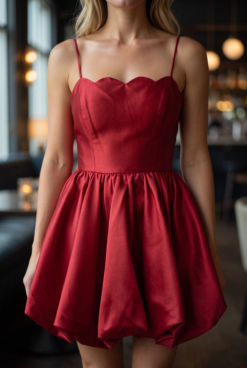 Close view of the red dress showing its scalloped neckline, fine straps, bodice seams and satin sheen.