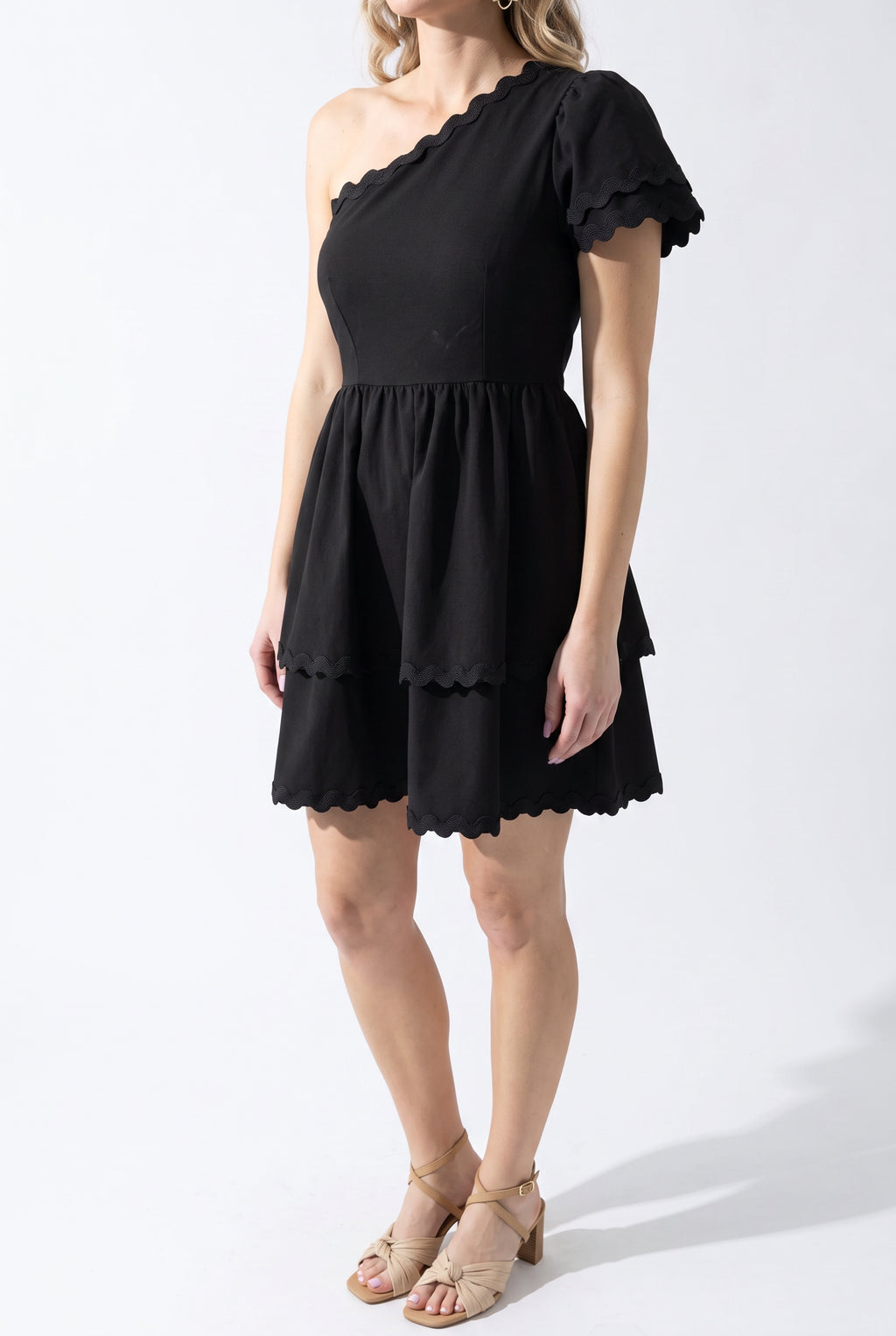 Three-quarter view of the black mini dress showing the puff sleeve, asymmetric neckline, and A-line flare.
