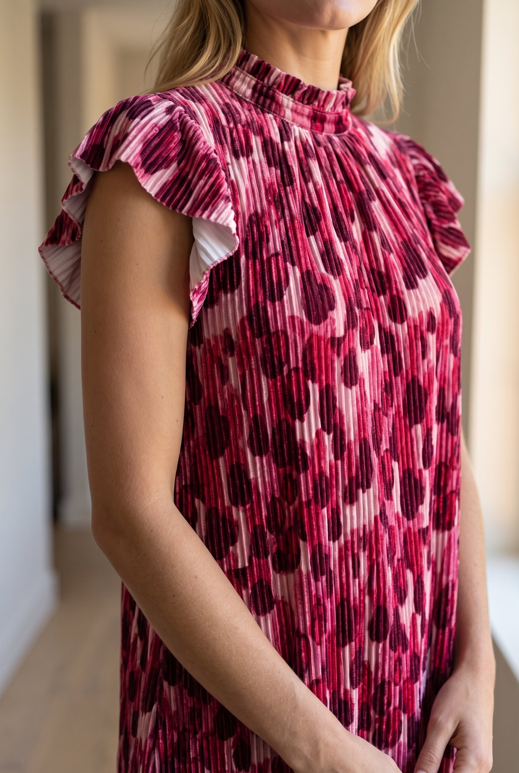 Close view of the pink dress showing vertical pleats, velvet-like sheen and layered flutter sleeve.
