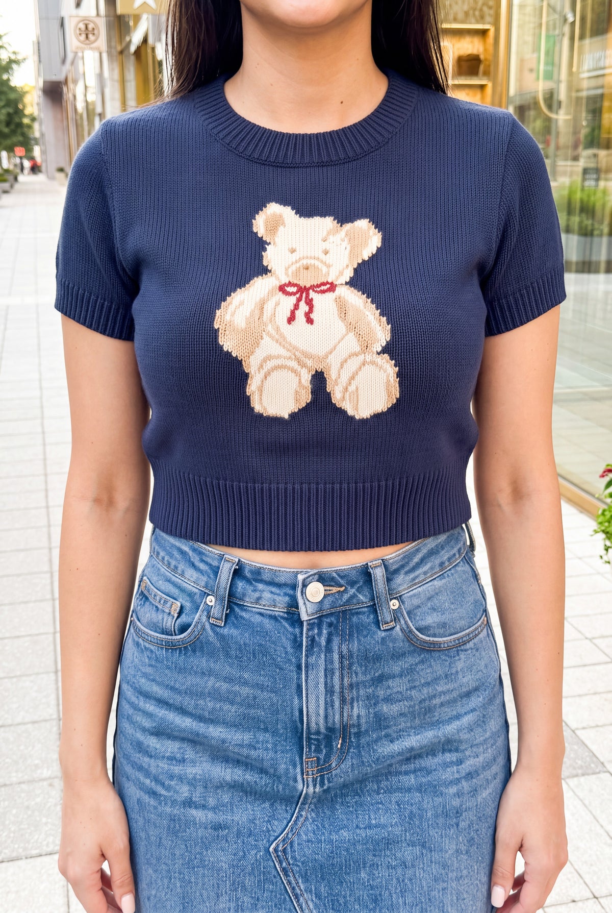 Close detail of the teddy bear motif, navy knit stitches, and ribbed hem of the cropped sweater top.