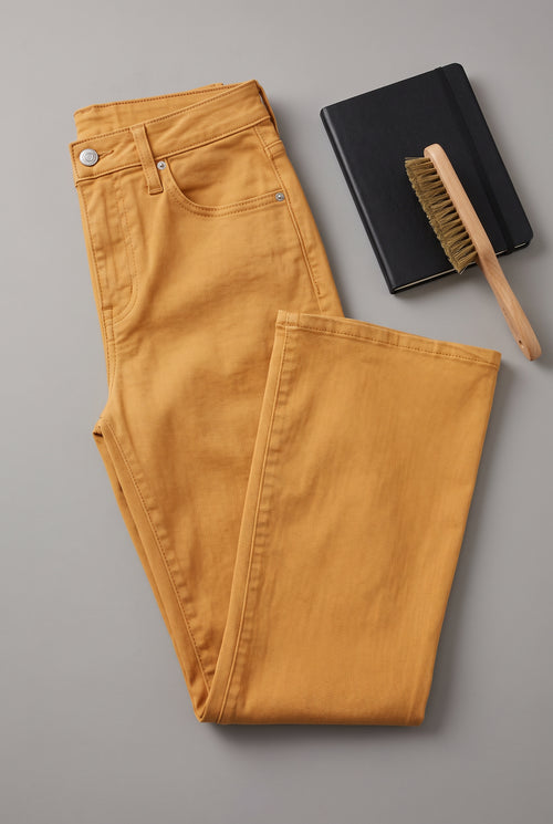 Gold kick-flare pants detail showing the denim texture, waistband hardware, stitching and raw-cut hem.