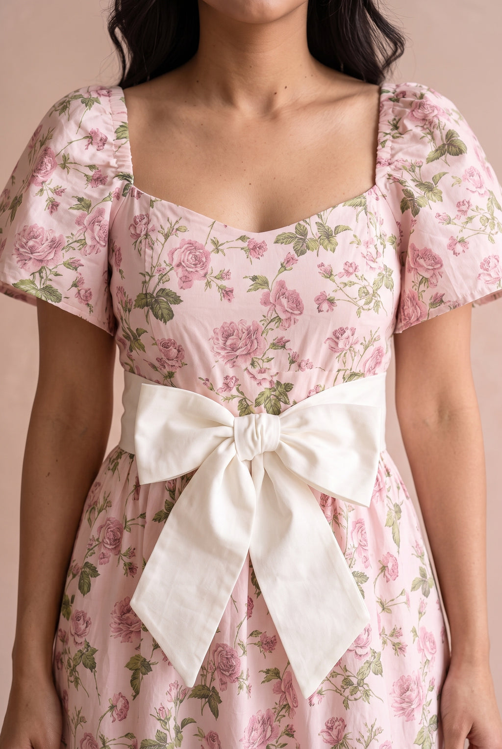 Close view of the pink floral dress showing its flutter sleeve, matte print and ivory bow belt.