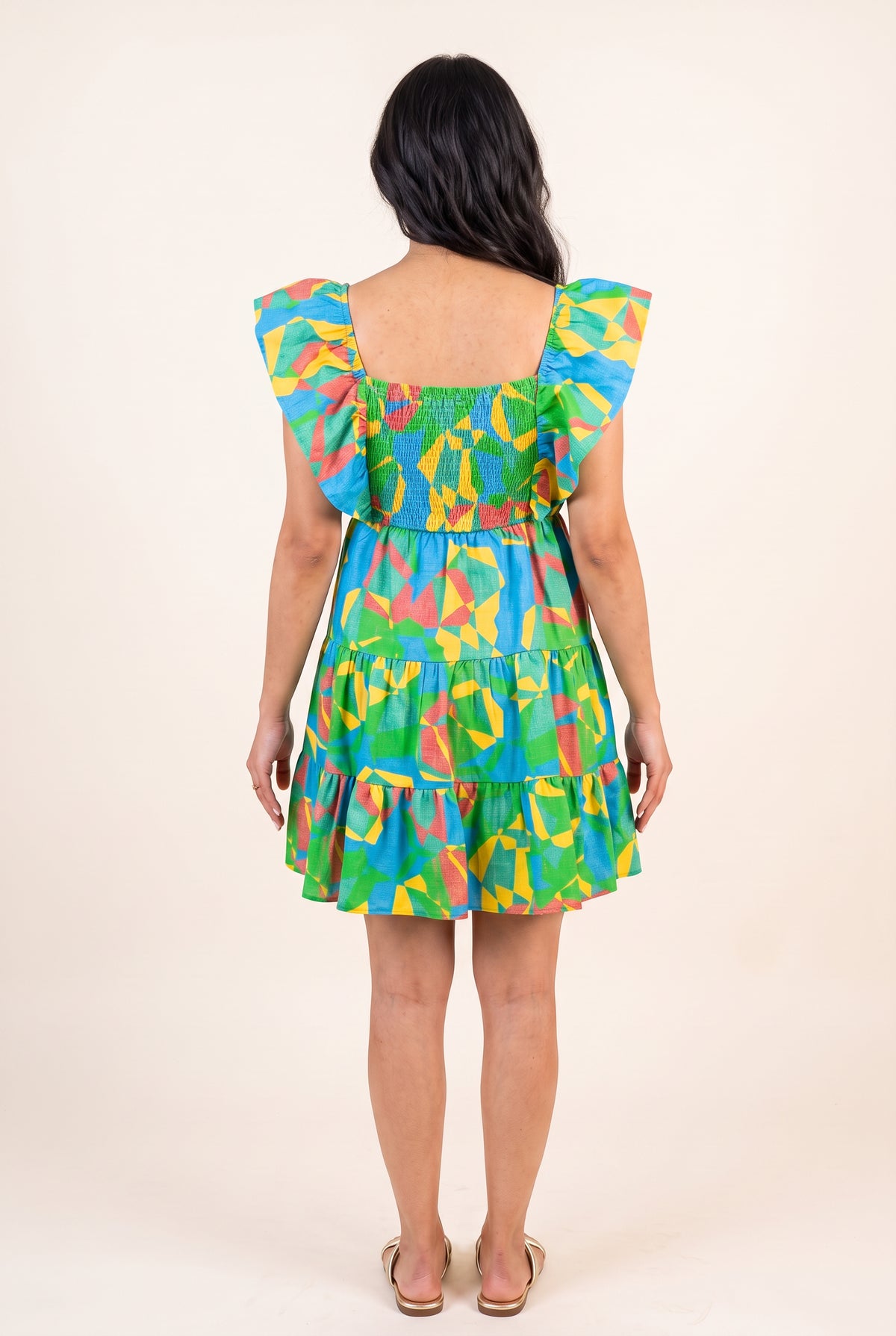 Back fit of the geometric mini dress showing its square back, smocked bodice and tiered skirt.