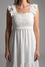 Close detail of the white dress showing crochet texture, ruffled straps, waist band, and woven skirt.