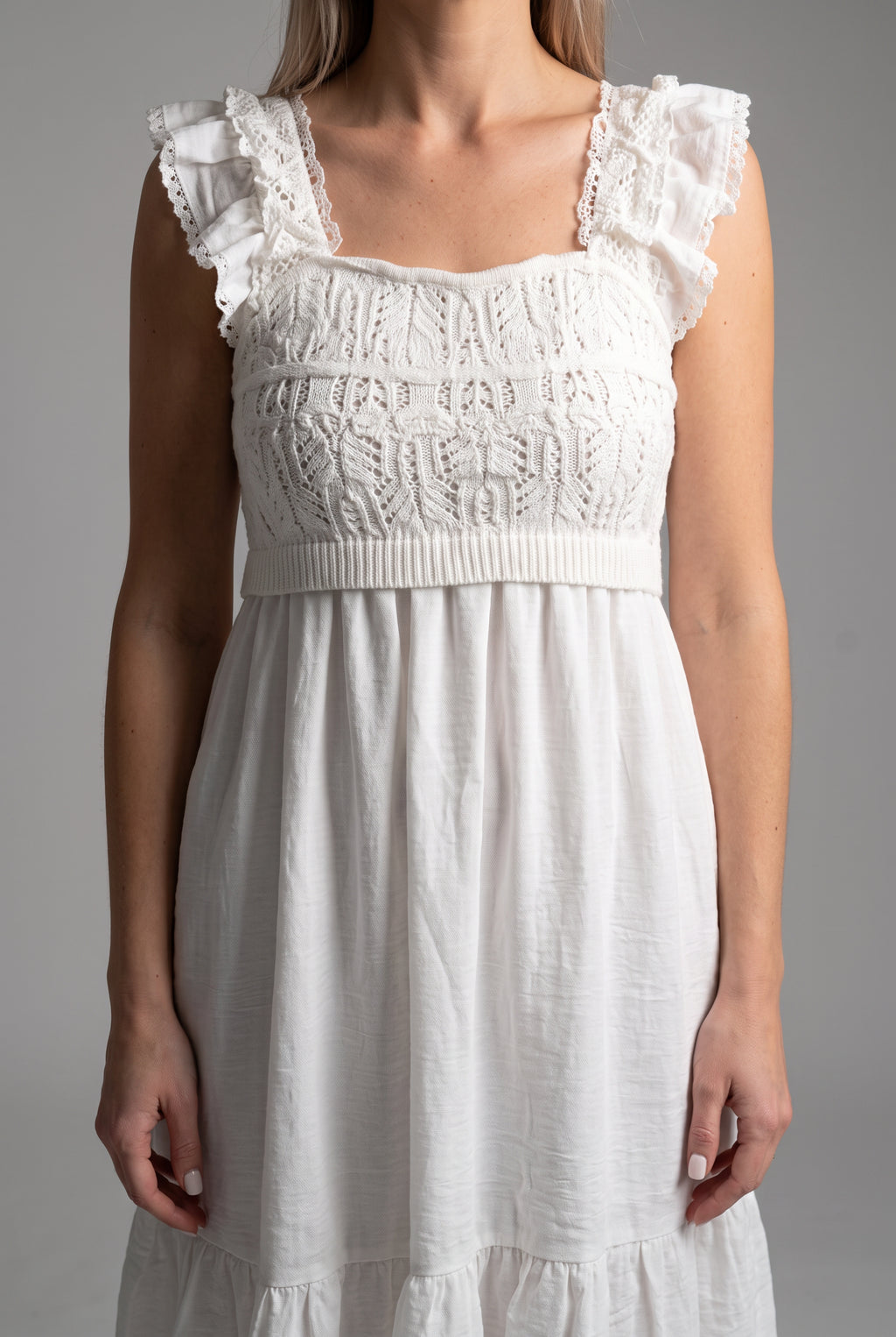 Close detail of the white dress showing crochet texture, ruffled straps, waist band, and woven skirt.