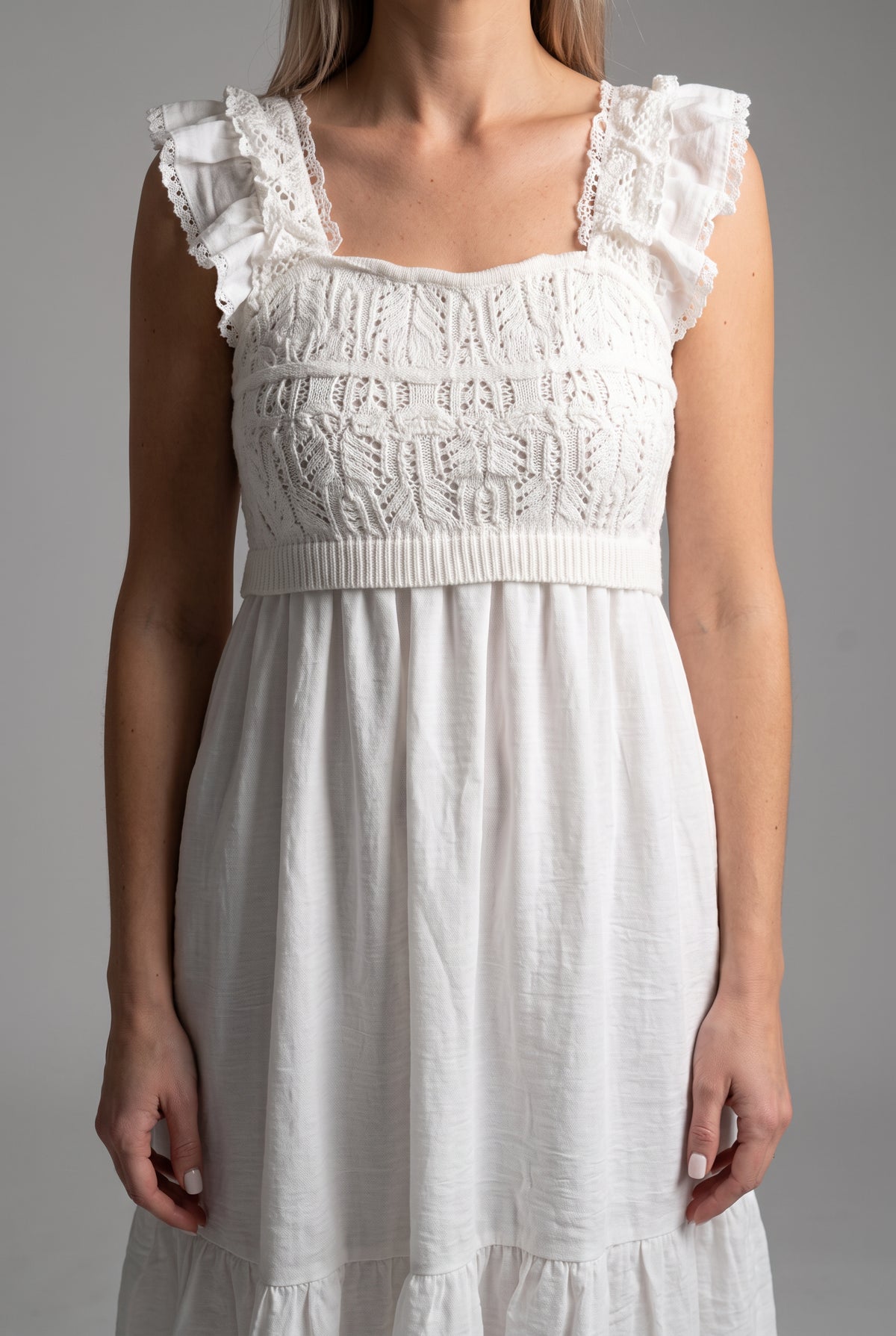 Close detail of the white dress showing crochet texture, ruffled straps, waist band, and woven skirt.