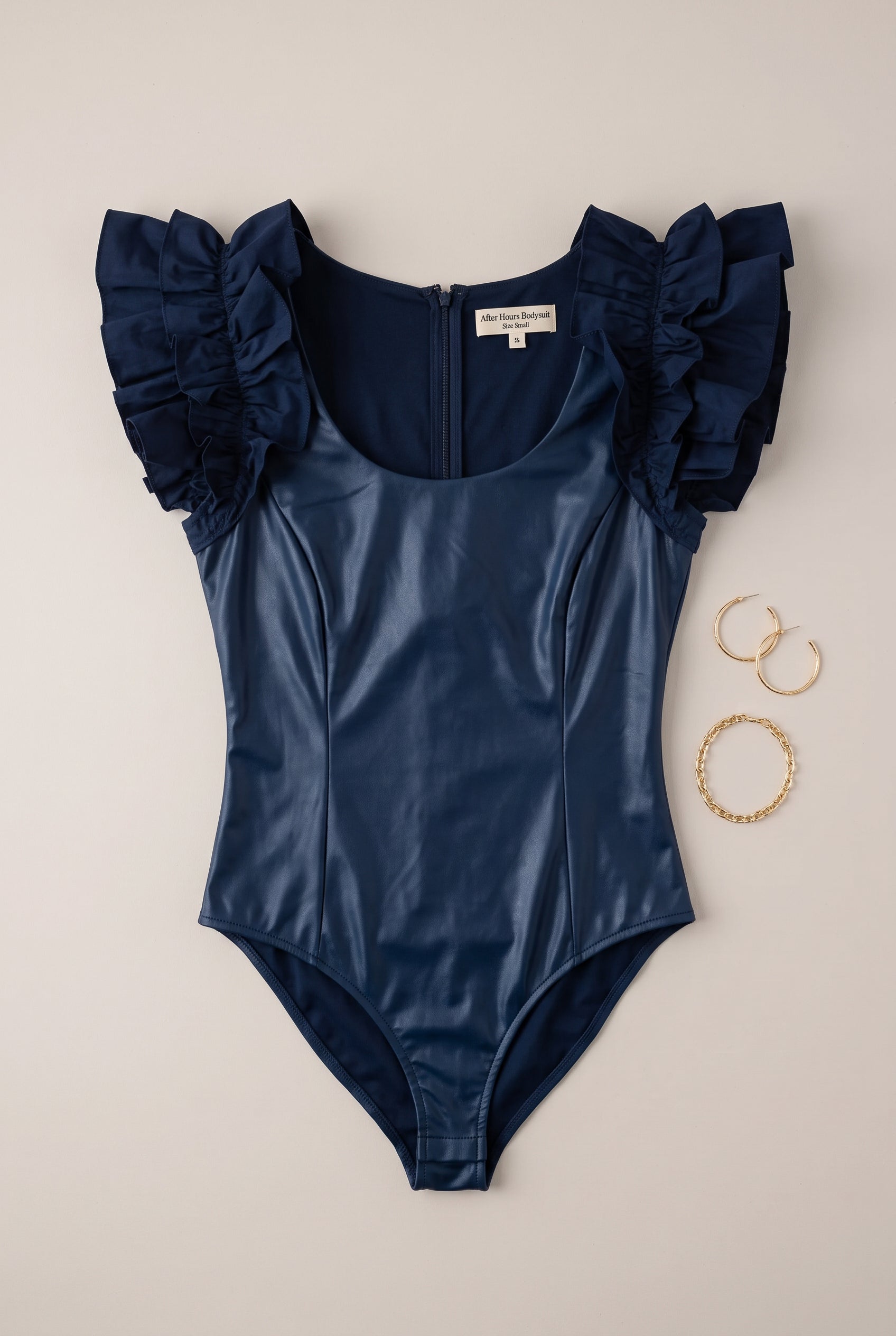 Lay-flat detail of the navy After Hours Bodysuit showing layered ruffles, faux leather and seams.