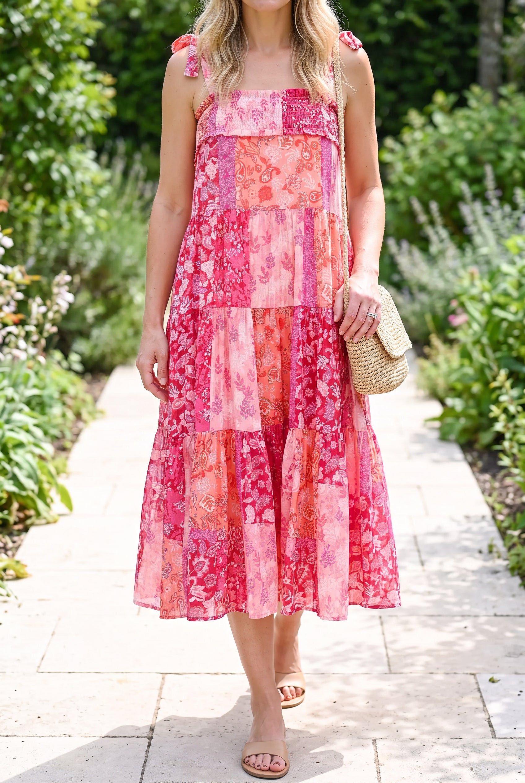 Pink patchwork shoulder-tie midi dress styled with sandals on a summer garden walkway